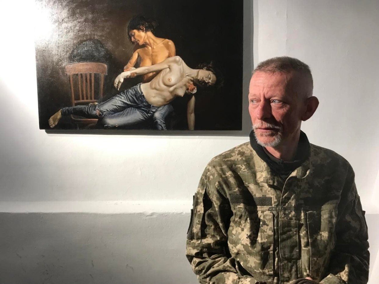 Artysta Genyk Rawski, który służy w Siłach Zbrojnych Ukrainy, na tle swojego obrazu